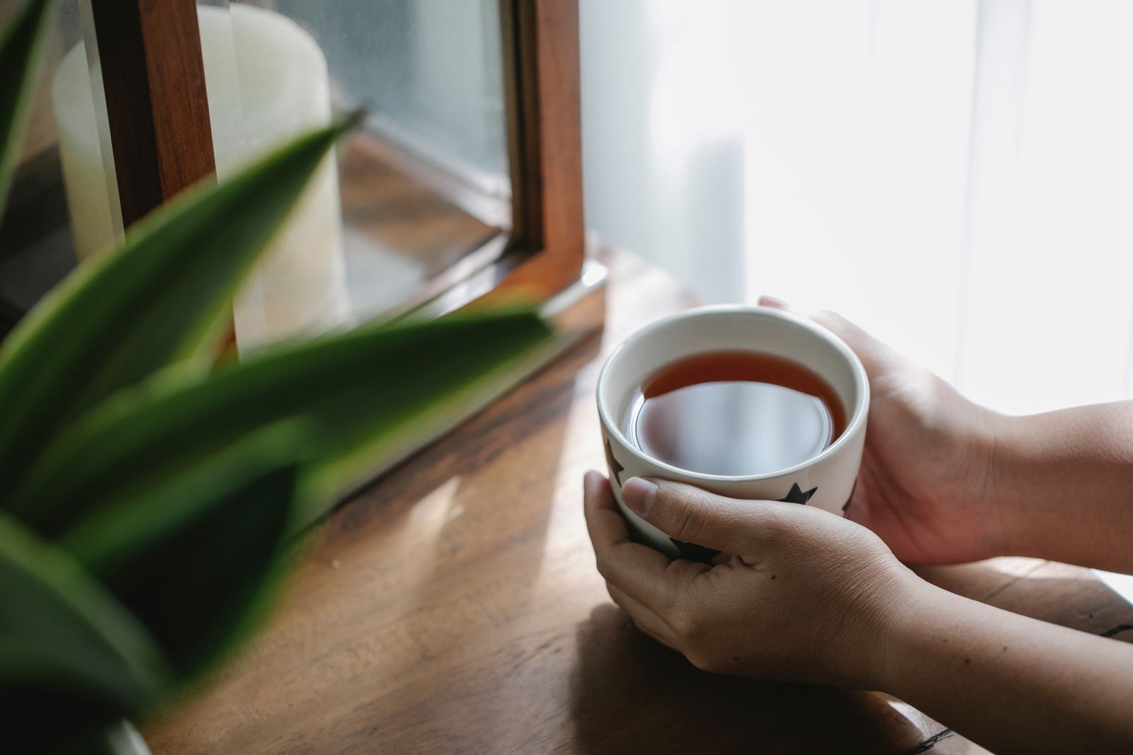 Deux mains autour d’une tasse de tisane près d’une fenêtre